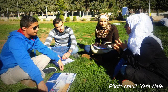 Four young adults sitting on the grass in discussion.