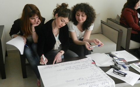 Three women sitting on a couch, working on a whiteboard sheet together.