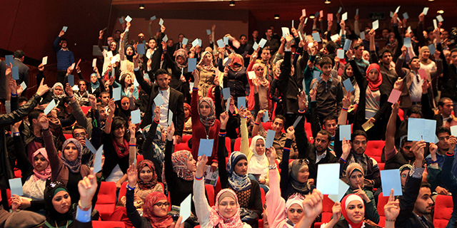 Muslim men and women voting in an assembly by raising white cards.